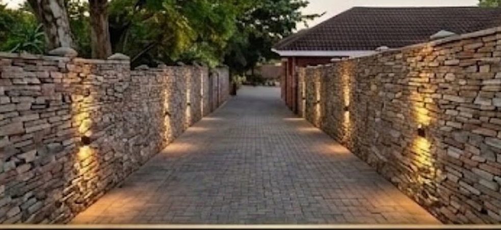 Long paved walkway between two stacked-stone walls with accent lighting