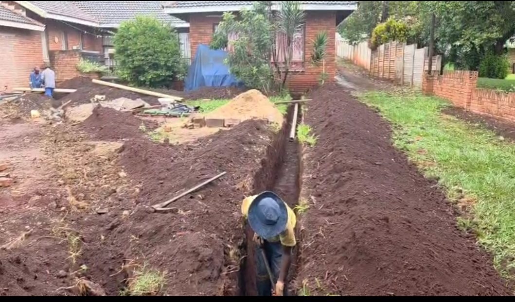Plumber digging a trench for new pipe installation at a residential property
